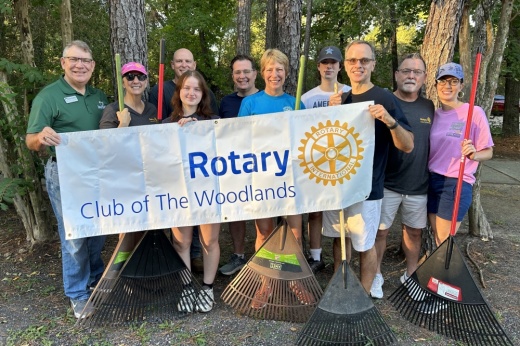 A group of people standing outside with rakes hole up a Rotary banner