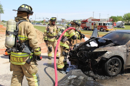 Ethan Green (center), a 21-year-old League City volunteer firefighter, puts out a car fire with other firefighters April 2. (Rachel Leland/Community Impact)