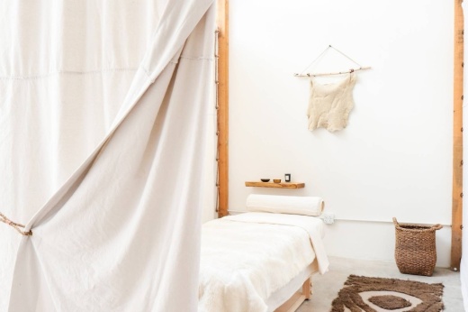A linen looking curtain pulled back to reveal a bed covered in neutral linens.