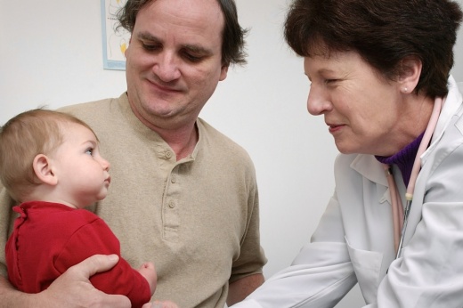 A man holds a baby while a physician performs a checkup.