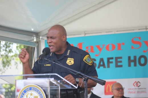 a man in a police uniform speaks into a microphone at a podium at under a tent outdoors
