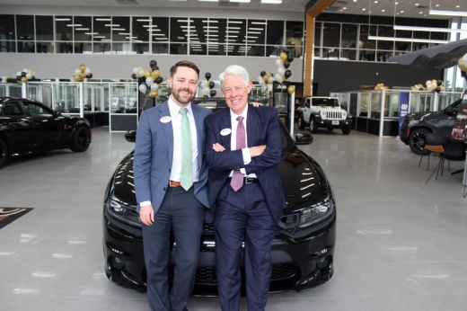Two men leaning against a car in a car dealership showroom.