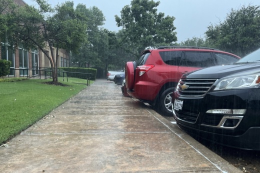 Rain hitting the cars and sidewalk in a parking lot during a thunderstorm