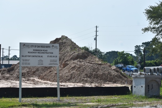 a sign alongside a mound of dirt and road construction