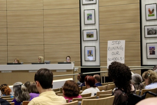 Many meeting attendees held signs from the audience with messaging directed at the board throughout the June 17 meeting. (Danica Lloyd/Community Impact)
