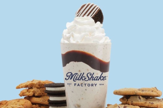 Milkshake with band of chocolate dividing the milkshake, topped with whipped cream and a cookie in a cup with Milkshake Factory logo.