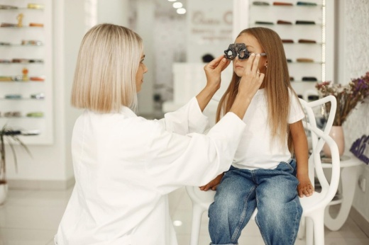 a woman giving a girl sitting in a chair an eye exam