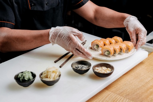 The hands of a chef are shown as they organize sushi and accoutrements on a tray.