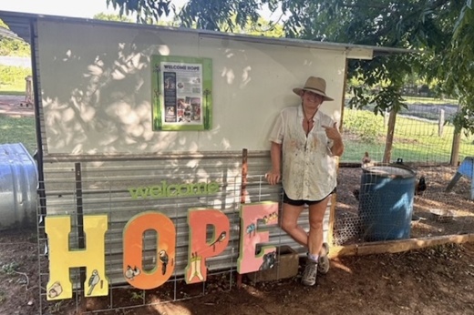 Jana Lynch poses in front of the chicken coop at the farm with her "Hope" sign.