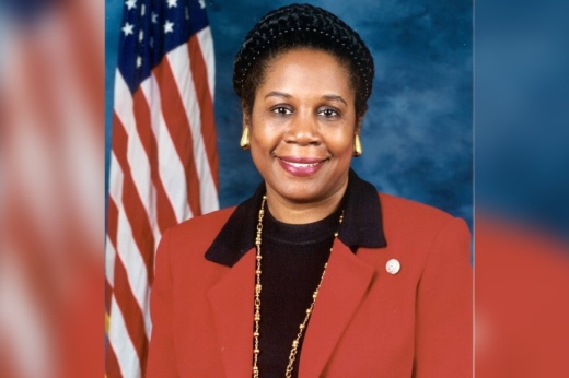 a headshot photo of a woman in a red jacket in front of an American flag