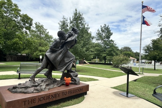 The sculpture is shown, with Harriet Tubman on the right guiding a young person behind her, with arms outstretched toward the United States and Texas flags.