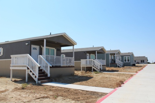 Gray and white trailer homes side by side along a road.