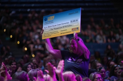 A teacher raises a large check above her head while standing in a crowd of people