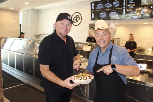 Picture of two people showing a dish at their restaurant.