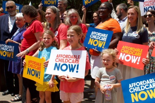 Families hold affordable child care now signs in front of the Travis County Courthouse