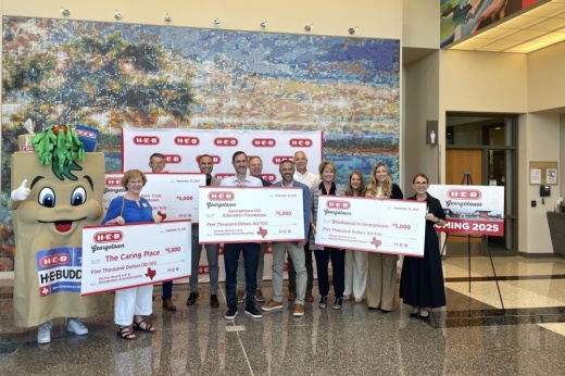 Nonprofit representatives hold out four large $5,000 checks inside a building.