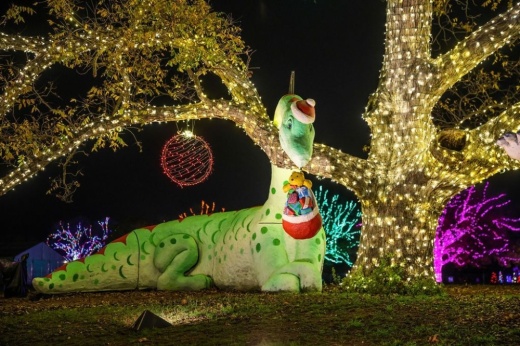 A holiday light display features a dinosaur dressed up as Santa Claus