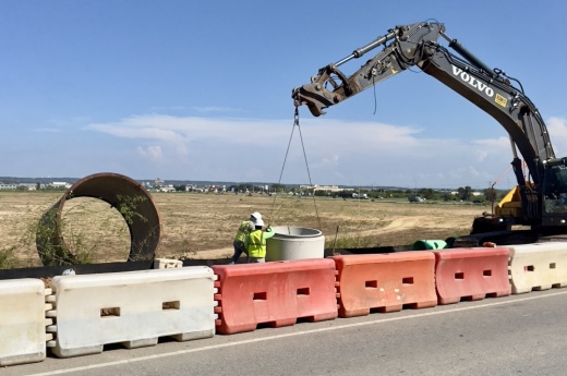 Workers move a piece of pipe into the ground.