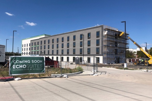 Building under construction with Echo Suites banner attached to a construction fence.