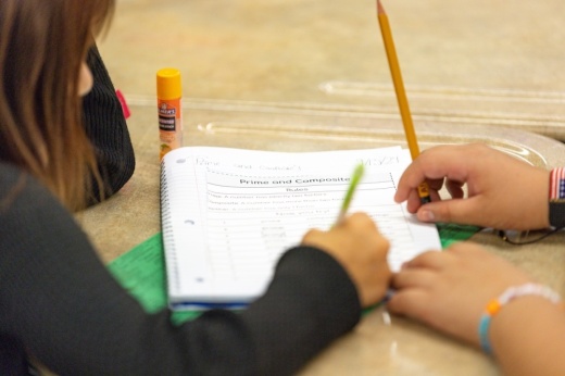 Two students lean over a desk with a worksheet reading, "prime and composite numbers"