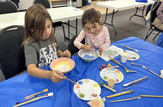 Two children sit side by side and paint bowls at a previous painting party.