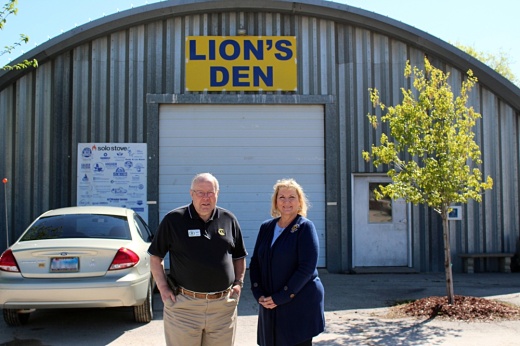 Male and female standing in front of curved-roof, metal building with Lion's Den signage.