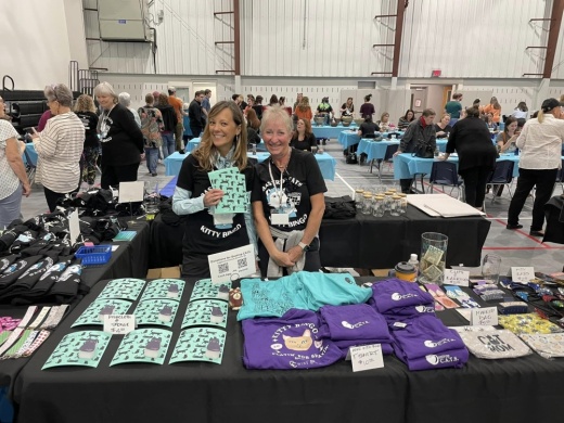 Volunteers are shown at a table selling shirts during an event.
