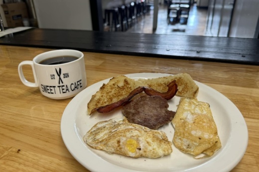 A white plate holds breakfast food with a Sweet Tea coffee cup is next to it.