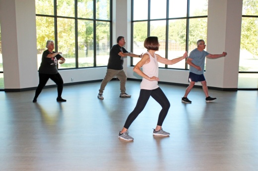 Group of people doing tai chi in a room with floor to ceiling windows.