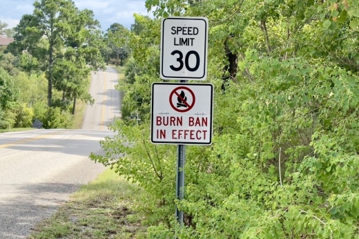 A burn ban sign is shown in Tahitian Village amongst green trees.