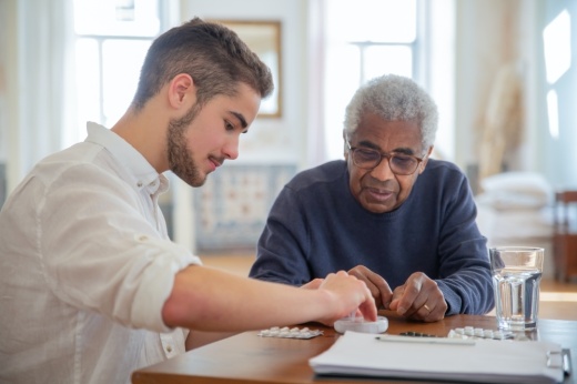 A younger man sits at a table with a senior citizen.