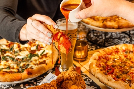Person drizzling sauce on a piece of fried chicken.