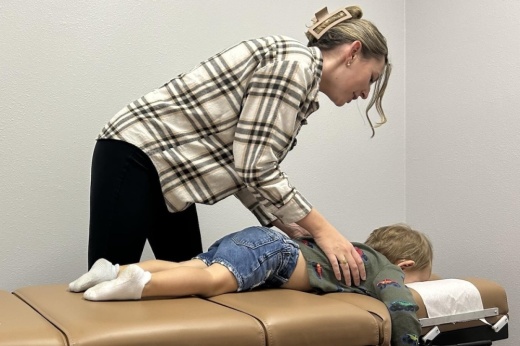 A chiropractor gives a physical assessment to a child laying on a table.