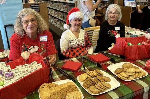 Three people host a table filled with cookies at a previous open house.