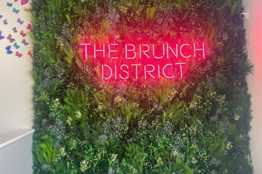 Greenery covered wall with The Brunch District pink neon signage.
