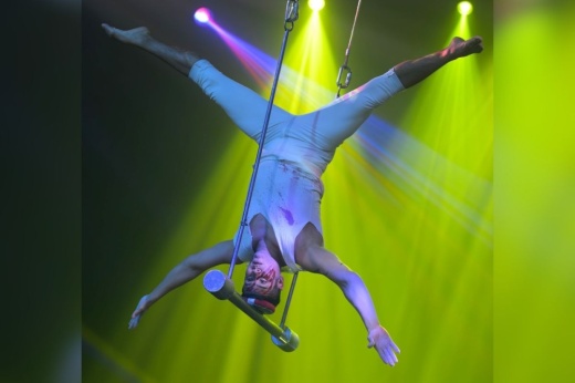 a performer hangs upside down in green spotlights