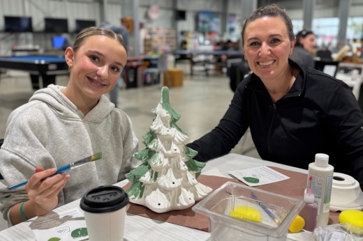 Two people smile while painting a Christmas tree.