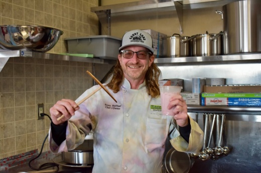 Male holding a crepe making tool and a smoothie while wearing a chef's jacket.