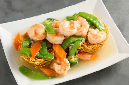 Dish with shrimp, pea pods, carrots and fried noodles in an off-white sauce in a white dish.