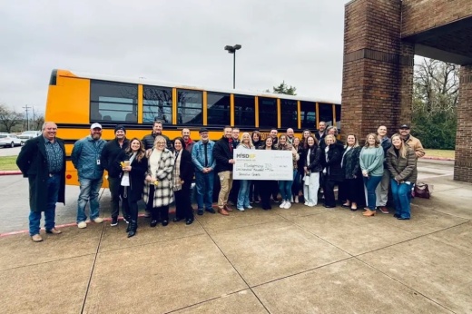 MISD Education Foundation members with a giant check in front of a school bus