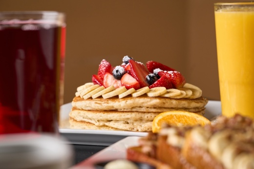 Stack of pancakes topped with berries on a plate flanked by two glasses of juice.