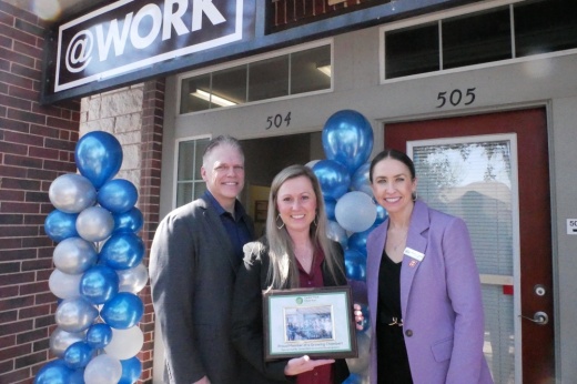 Three people smile in front of a building