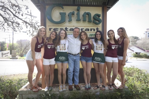 A photo of a man with staff around him in front of a sign that says Grin