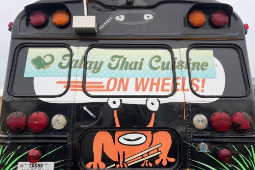 The back of a school bus that has been converted into a food truck with a frog-ish alien painted on it.