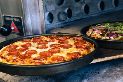 Cooked pizza in a metal pan next to an open oven.