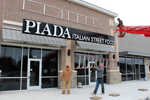 Exterior of building in a strip mall with PIada Italian Street Food signage being installed.