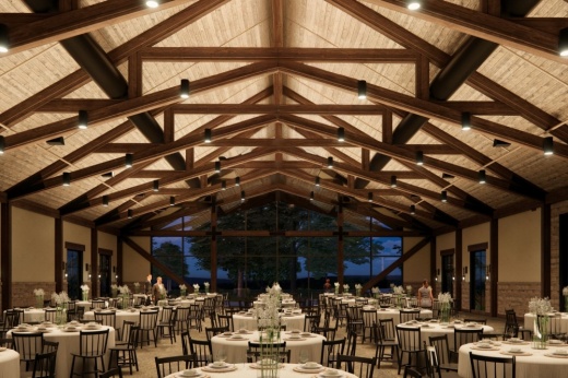 The indoor ballroom is shown with vaulted ceilings and exposed beams, dimmed lighting and rows of tables and chairs. In the background is a wall-sized window showing silhouettes of trees.
