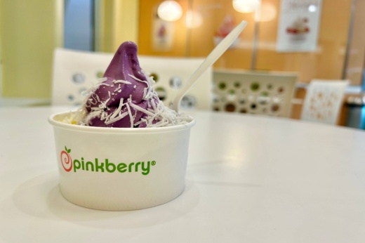 Pink yogurt with pineapple tidbits and coconut toppings in a cup with Pinkberry branding.