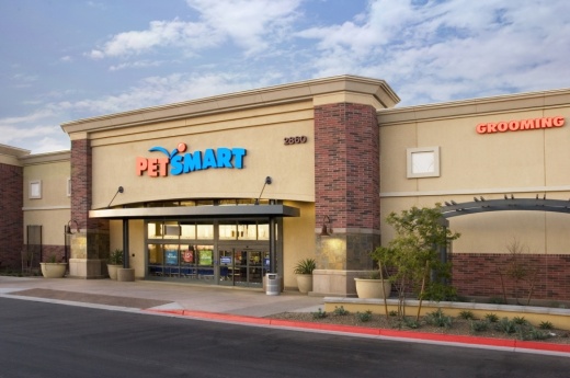 A brown exterior is shown of a typical PetSmart location, with the words Pet written in orange and Smart in blue. A cloudy sky is overhead.
