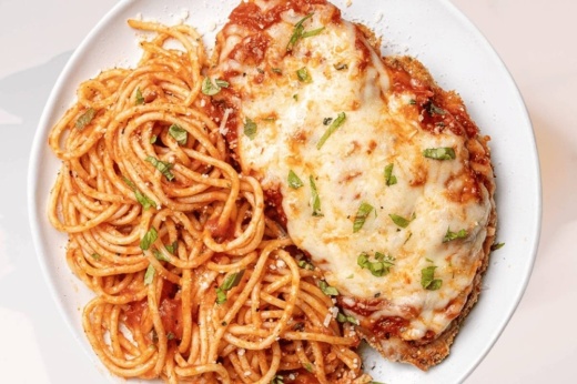 Marinara and cheese atop a piece of meat with a side of spaghetti noodles covered in red sauce.